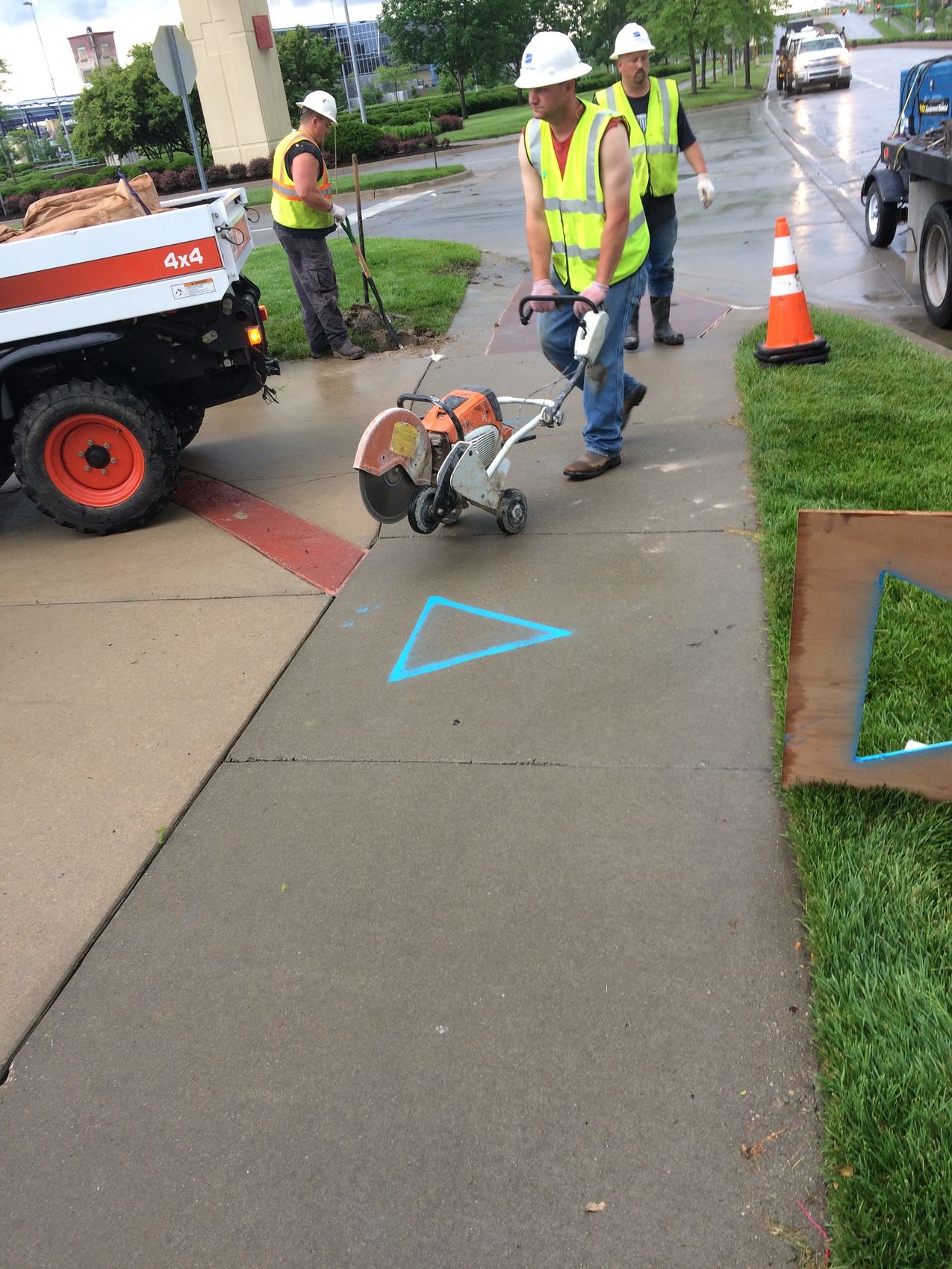 Crew cutting a sidewalk marked with a blue triangle.
