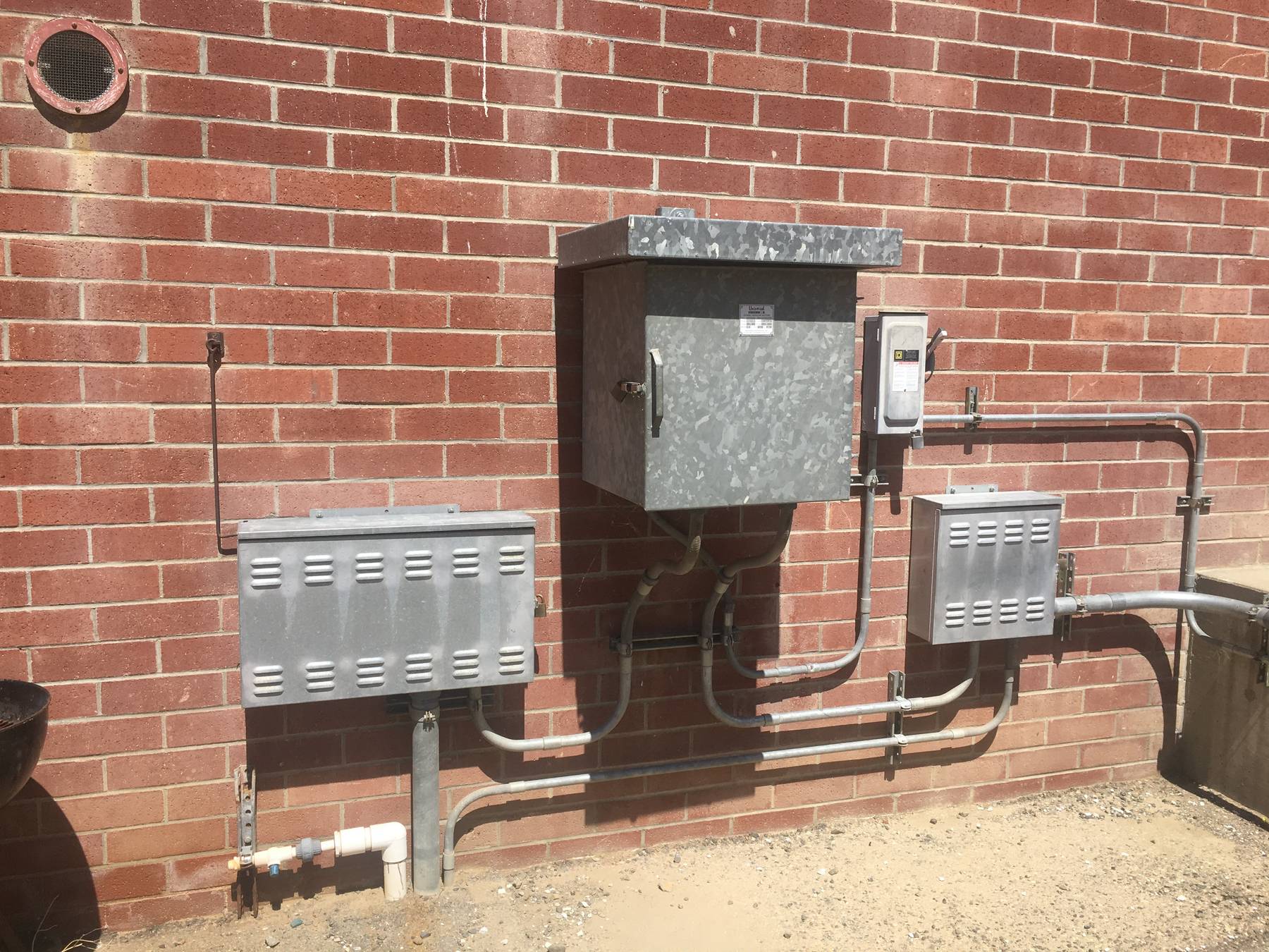 Galvanized rectifier and control cabinets with conduit mounted on a brick wall.