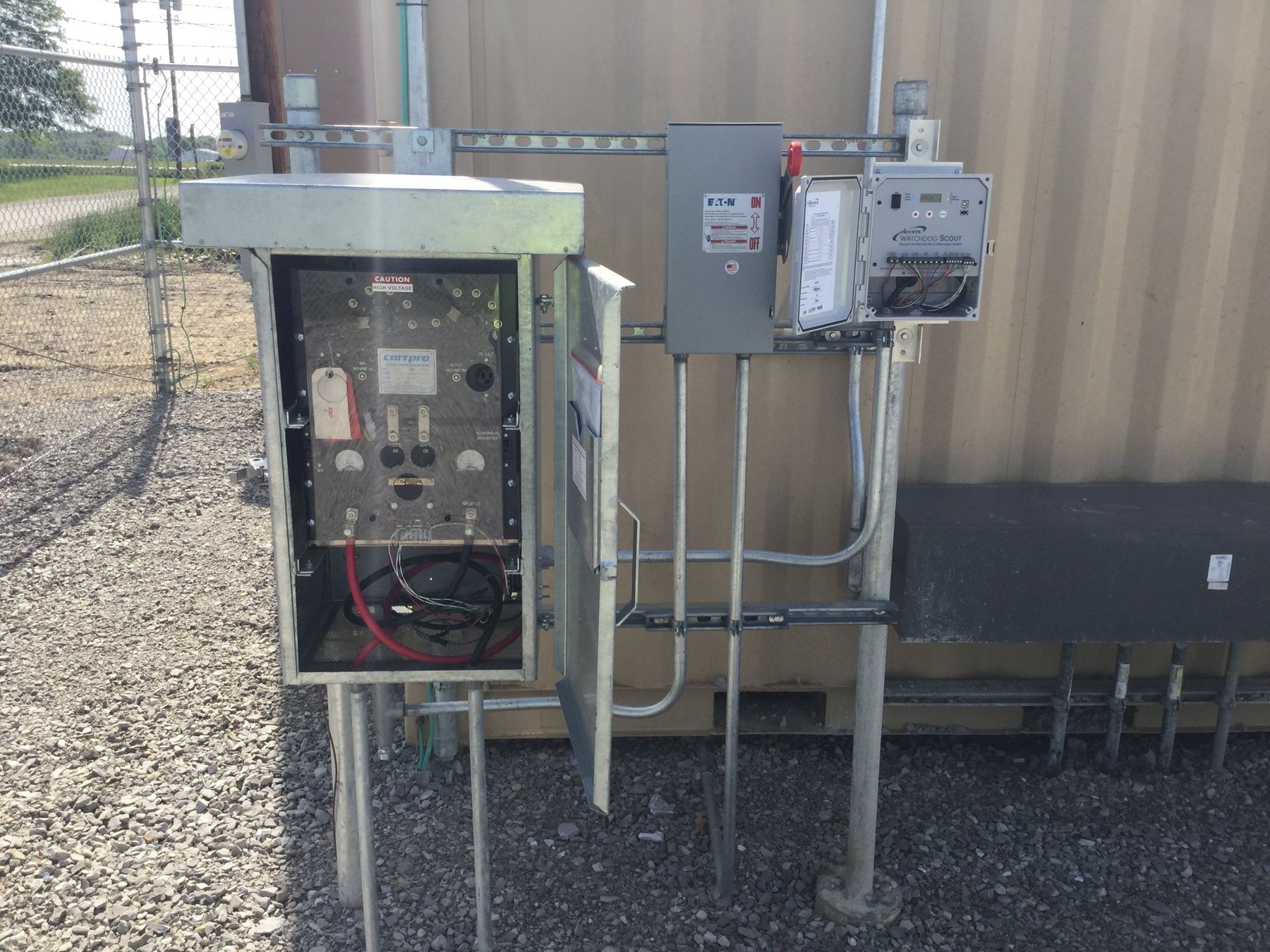 Outdoor cathodic protection rectifier cabinet with gauges, open, next to a remote monitor and disconnect switch.