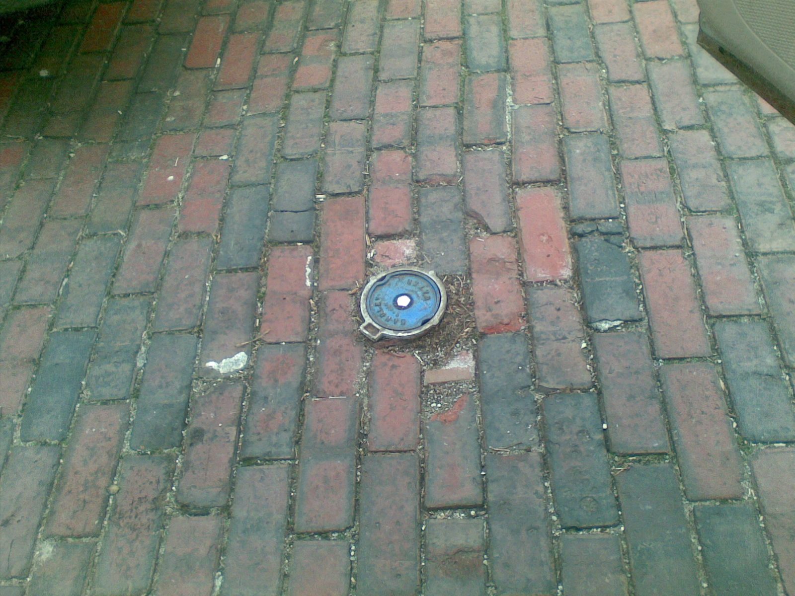 Round blue cathodic protection test station lid set flush among the bricks of a red brick road