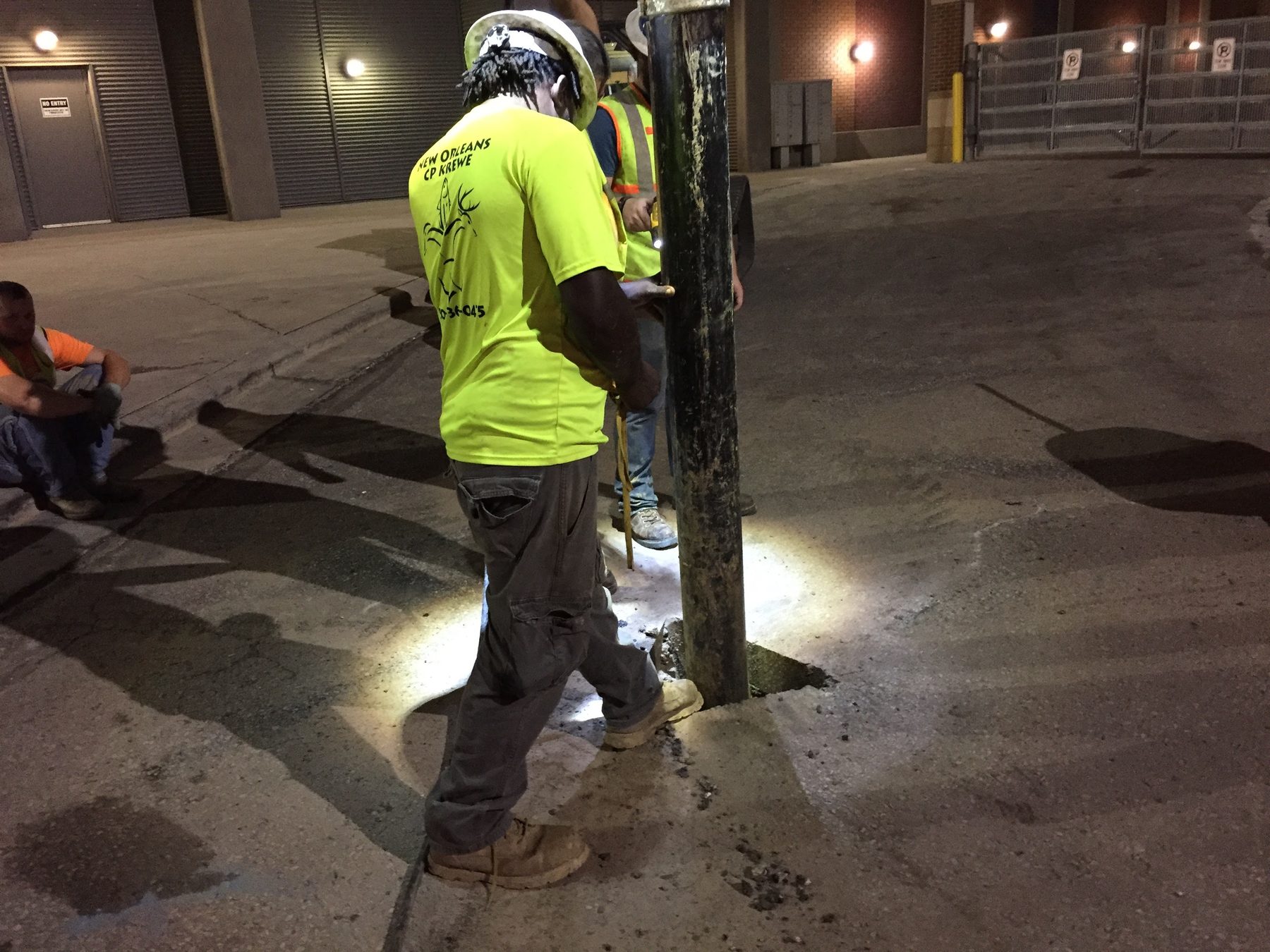 Crew working at night at the base of a pole with a cut in the pavement.