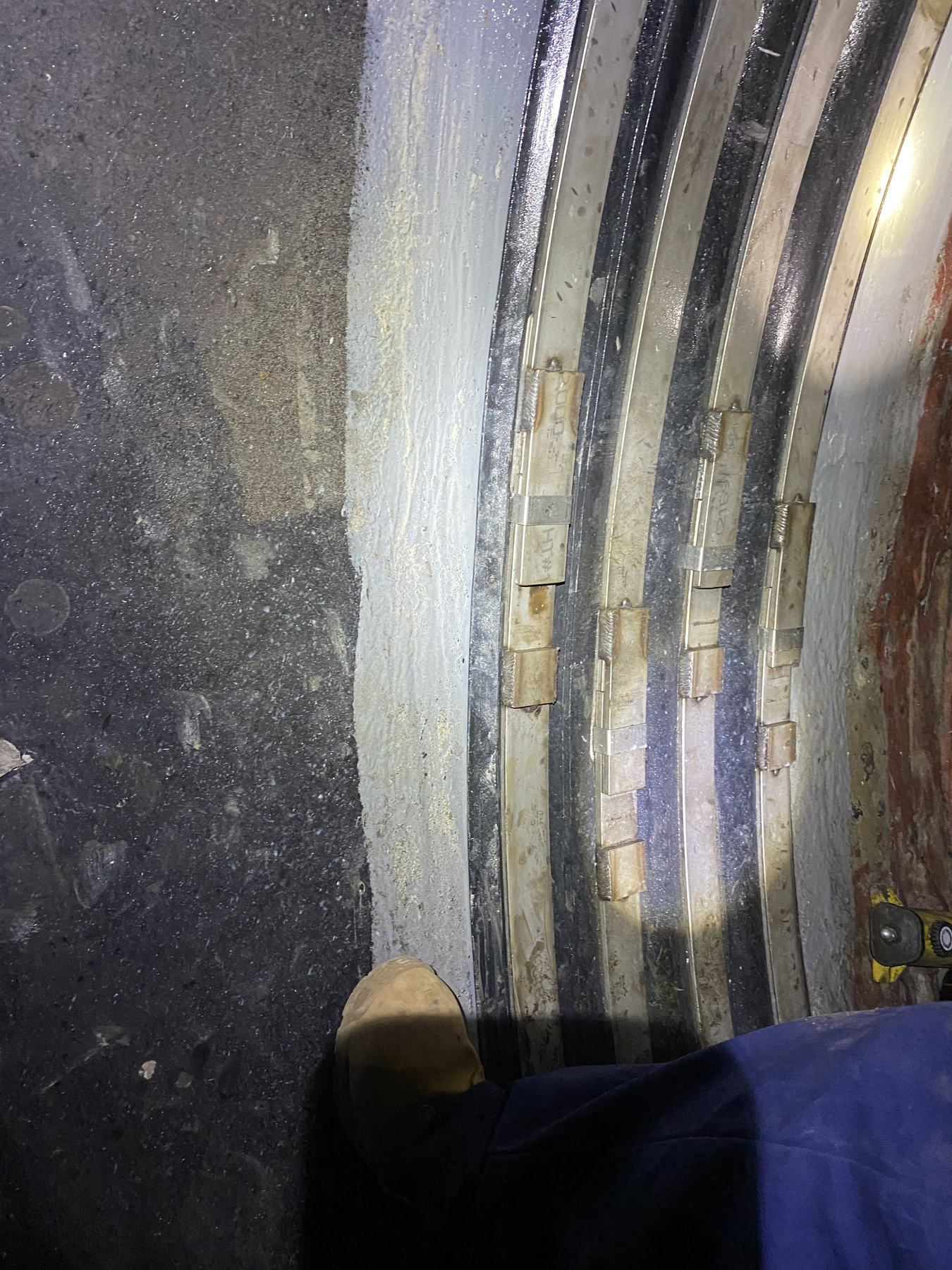 Steel bands and lining on the interior of a large-diameter pipe, with a work boot for scale