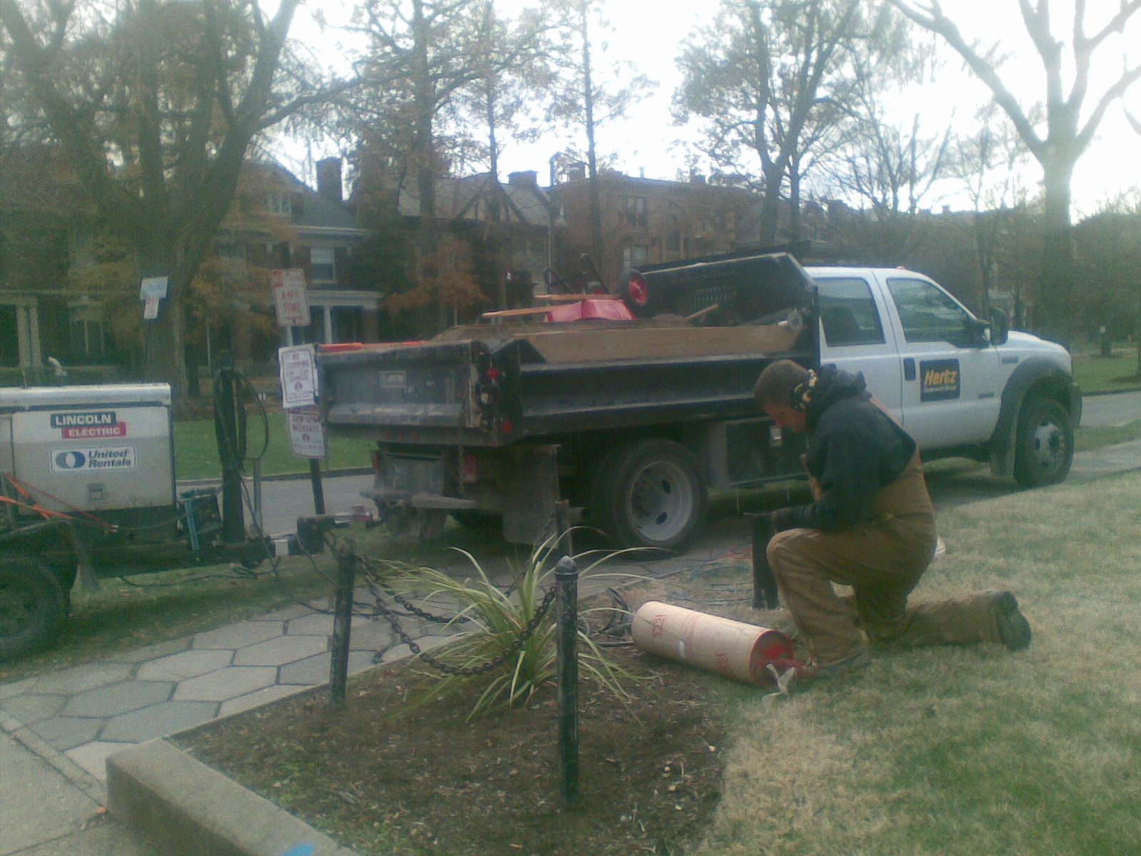 Worker kneeling on a lawn by a pickup and portable welder.