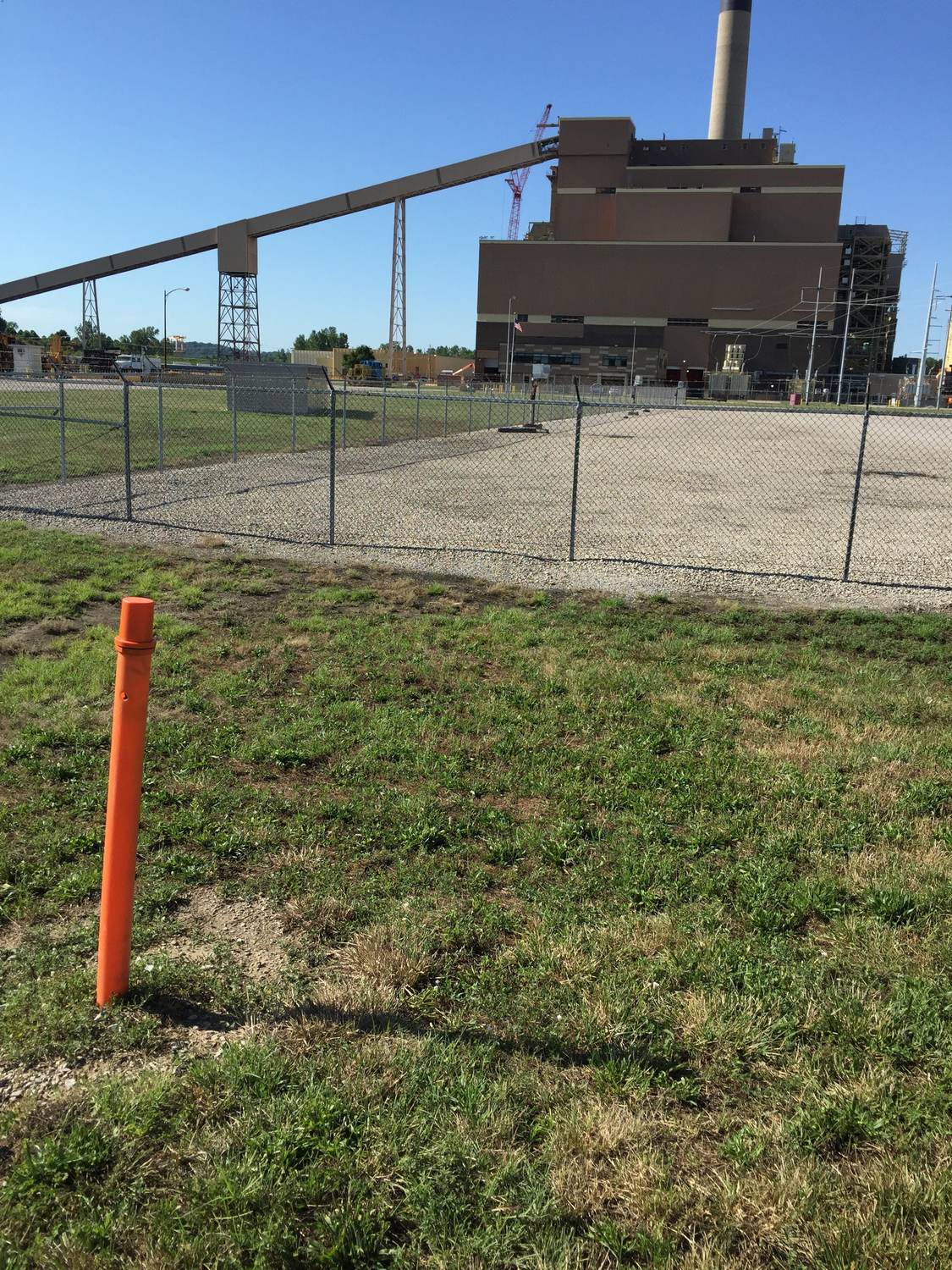 Orange marker post at a fenced industrial plant.