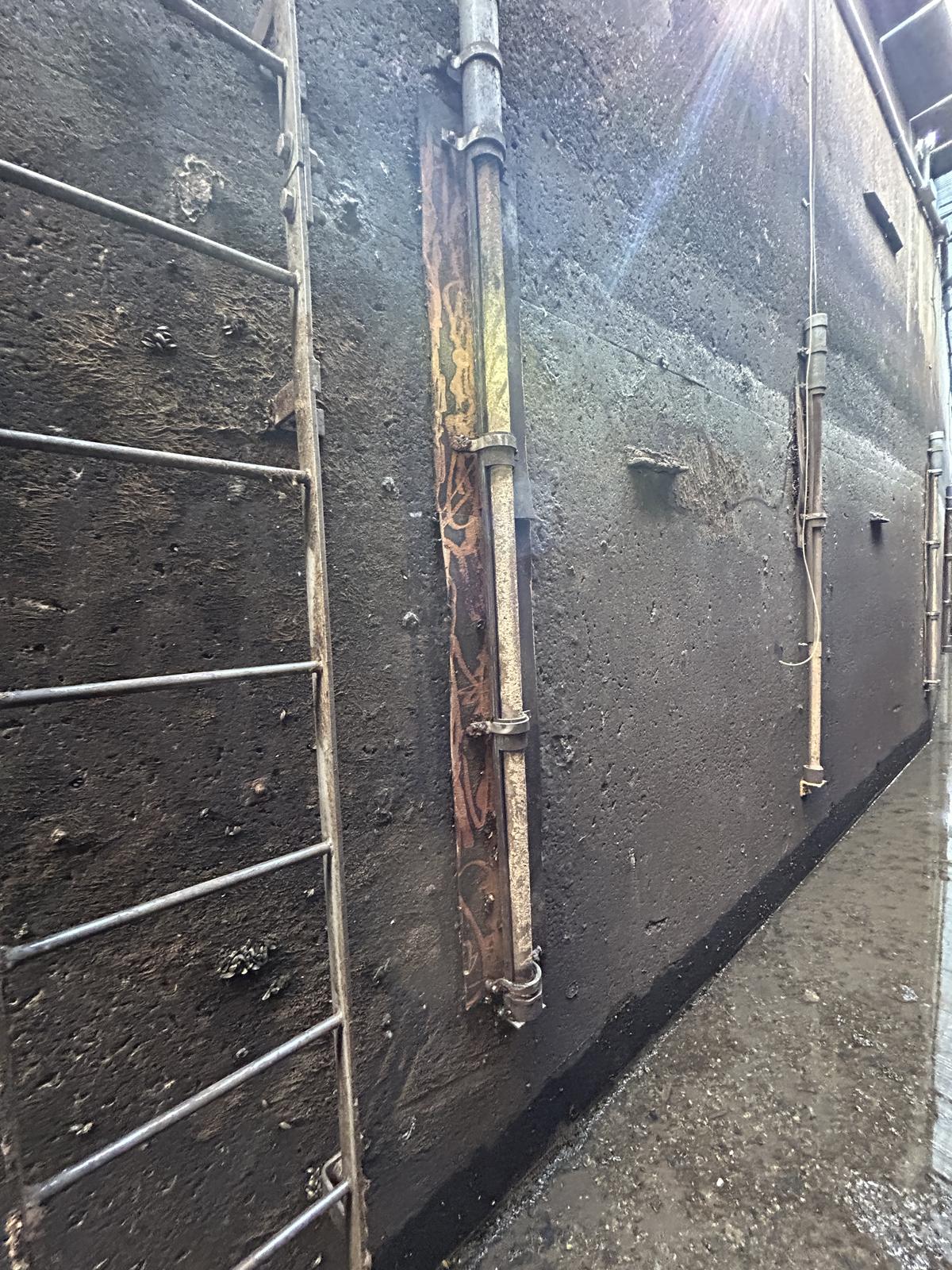 Interior of a steel tank with access ladder, piping, and rusted backing plate