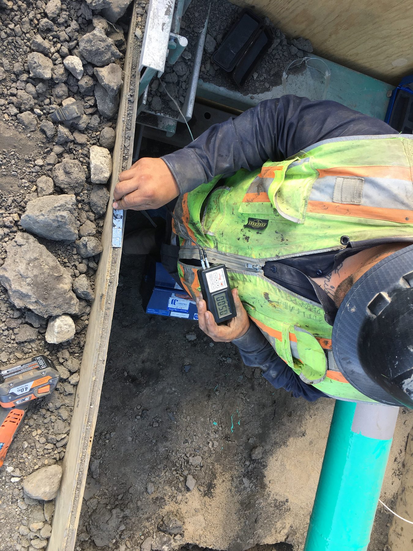 Worker in a trench with a digital gauge reading 0.50.