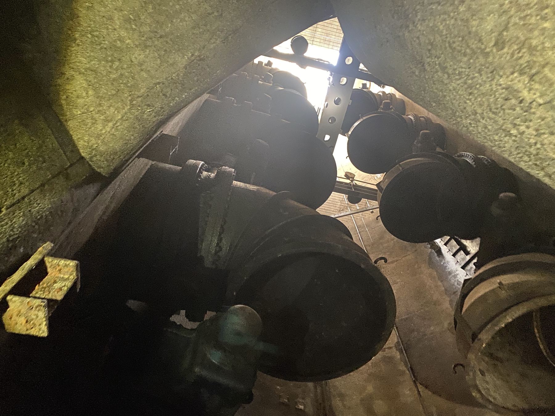 Looking up a deep utility vault with large flanged pipes toward a hatch of daylight