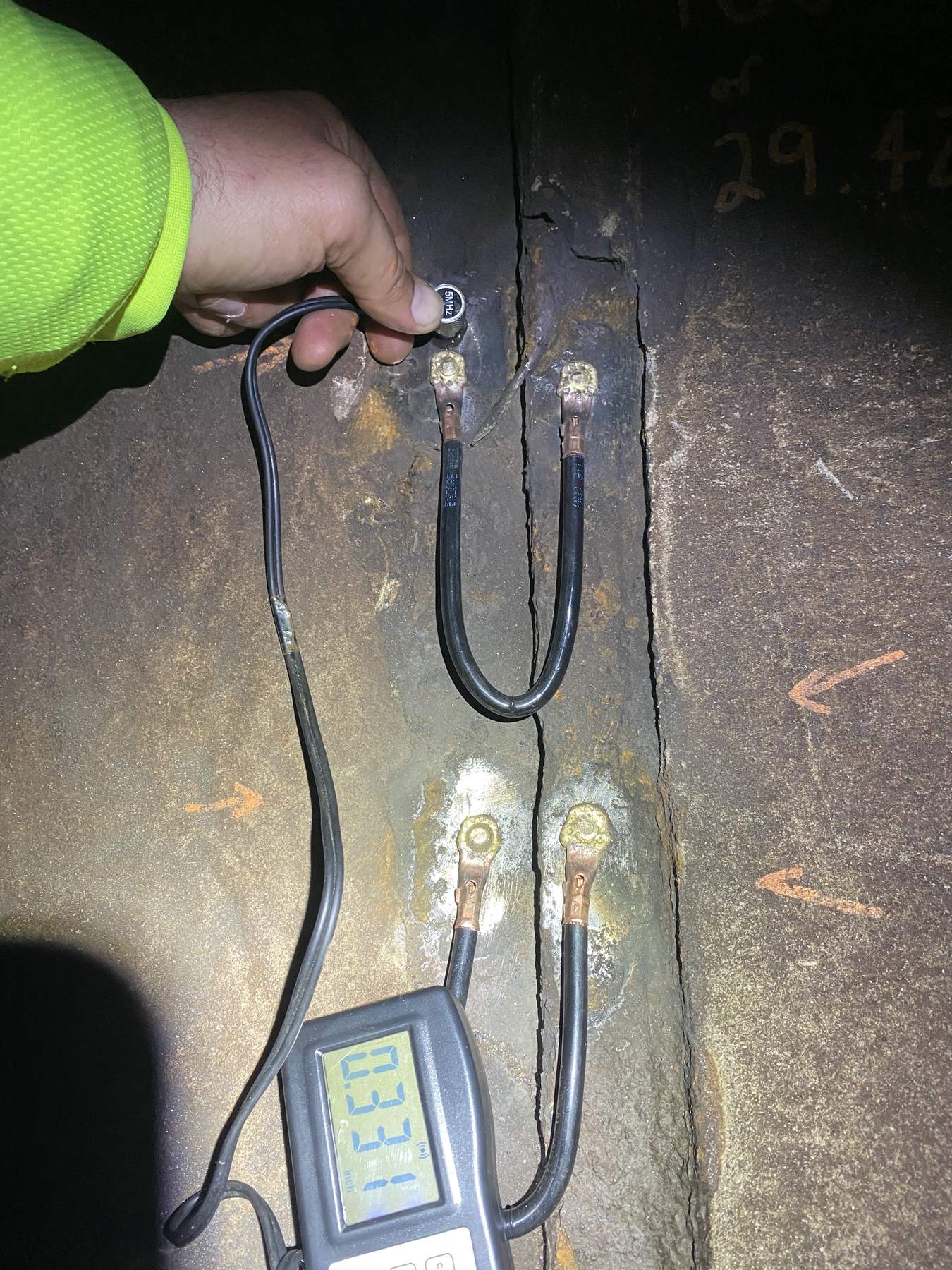 Ultrasonic thickness probe and digital gauge taking a reading on a steel surface.