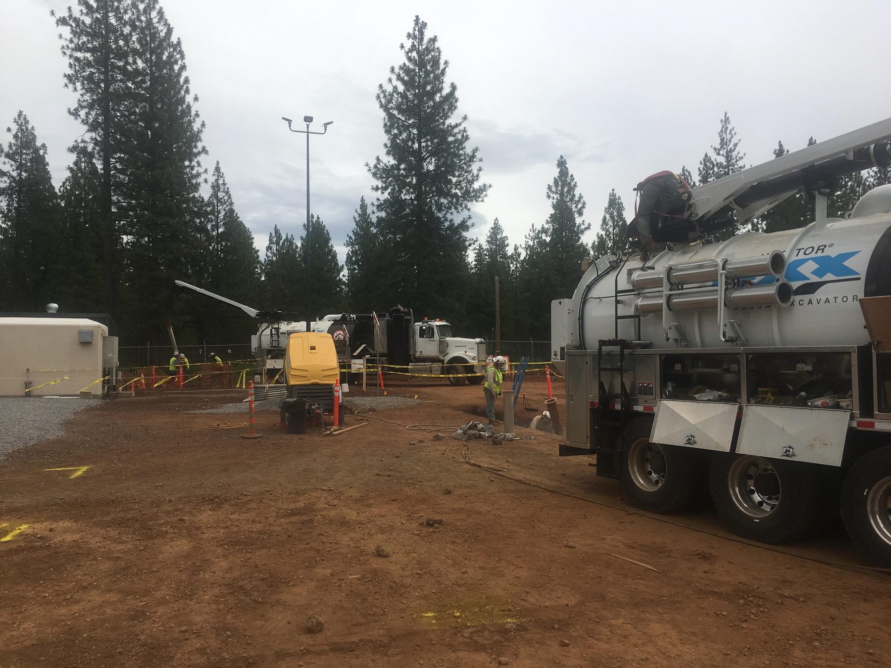 Vacuum excavator and crew on a dirt lot in the pines.