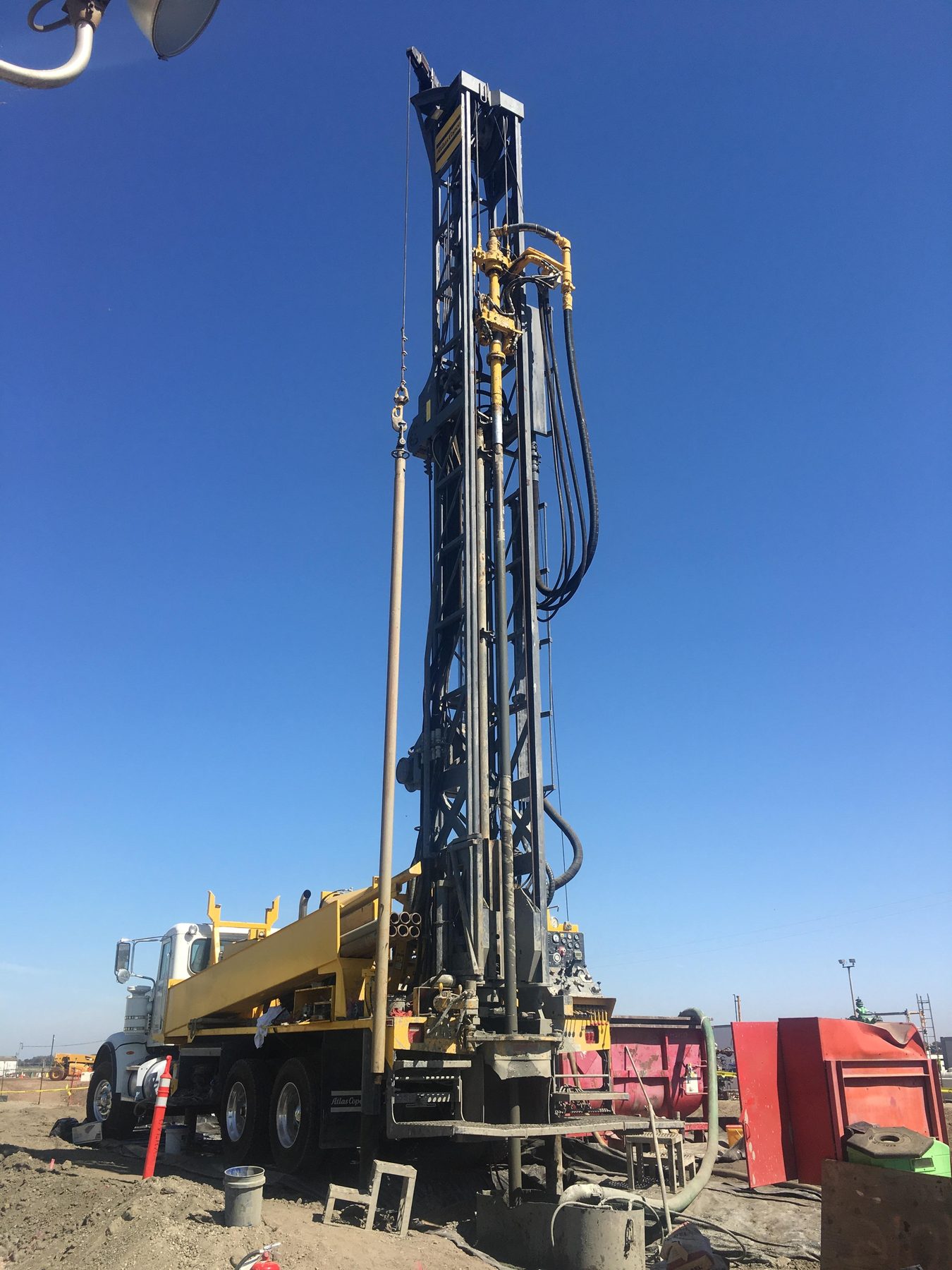 Truck-mounted drilling mast on a dirt site.